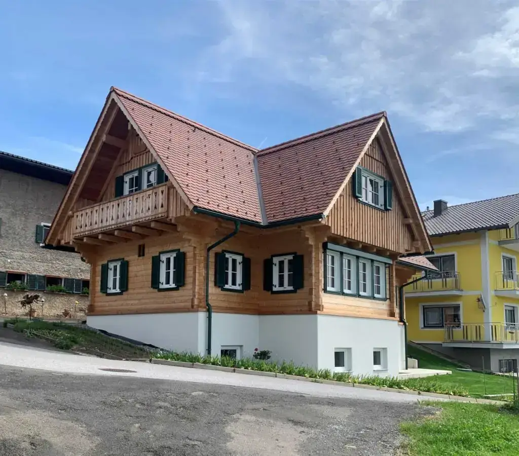 Traditionelles Holzhaus mit Satteldach, grünen Fensterläden und Balkon, in ruhiger Wohnlage.
