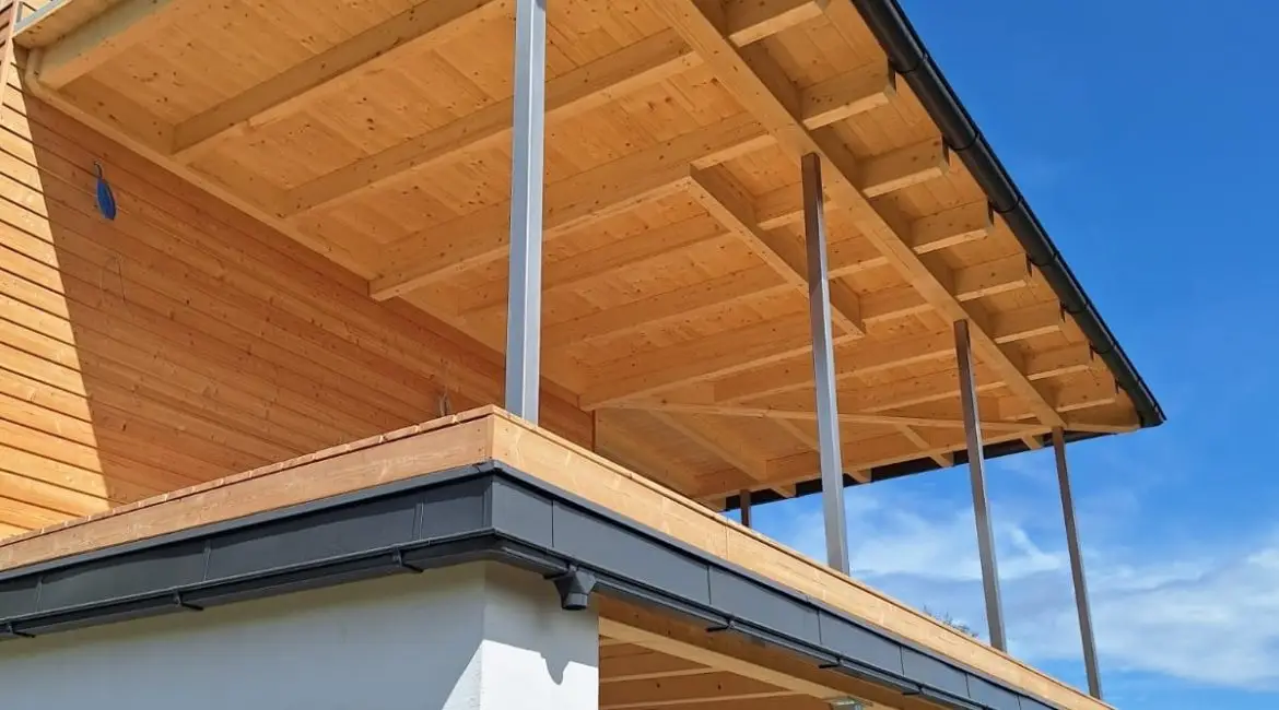 Holzhaus mit großzügigem Dachüberstand, sichtbarer Holzkonstruktion und schlanken Stahlstützen.