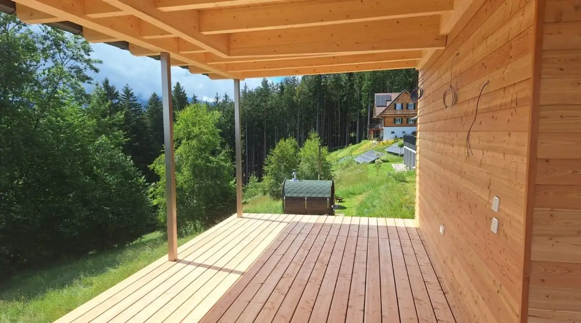 Modernes Holzhaus mit großzügigem Dachüberstand, sichtbarer Holzkonstruktion und schlanken Stahlstützen.