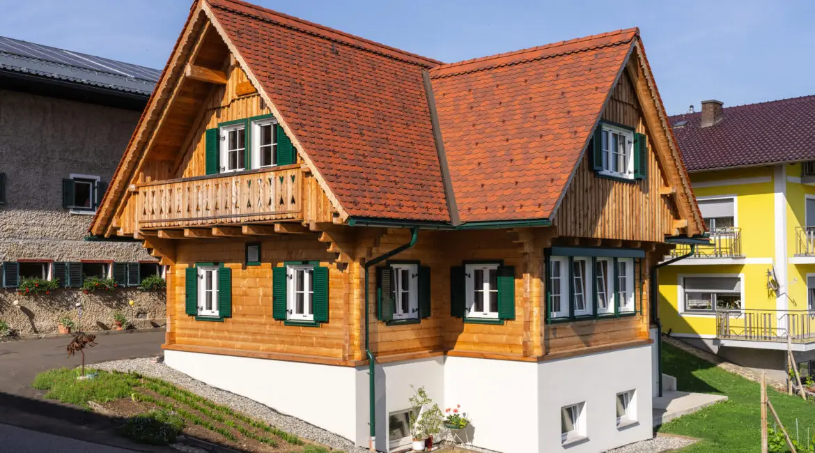 Traditionelles Holzhaus mit Satteldach, grünen Fensterläden und Balkon, in ruhiger Wohnlage.