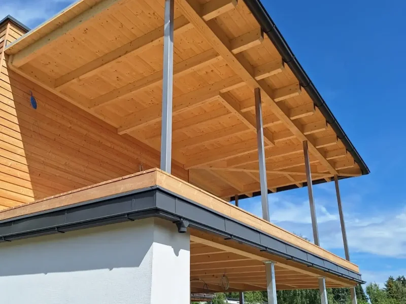 Holzhaus mit großzügigem Dachüberstand, sichtbarer Holzkonstruktion und schlanken Stahlstützen.