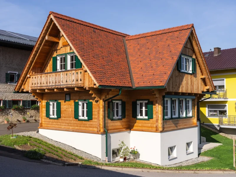 Traditionelles Holzhaus mit Satteldach, grünen Fensterläden und Balkon, in ruhiger Wohnlage.